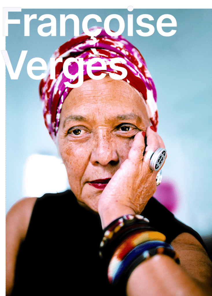 There is a portrait of Françoise Vergès, she is sitting in a colourful head scarf on the blue background. Her hand is tucked below her head. She is wearing colourful bracelets on her arm. The name of the speaker Françoise Vergès is written in white letters.